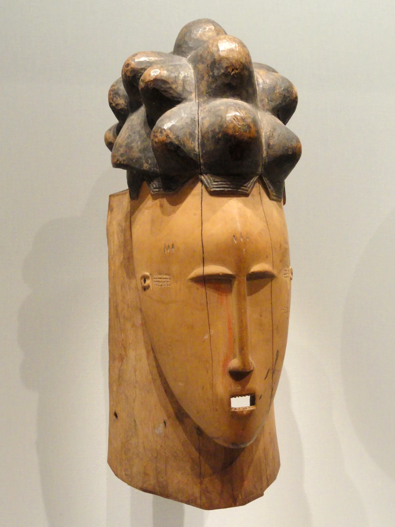 Masque féminin mblo baoulé en bois : coiffure sculptée et petites marques sur les tempes et le front.